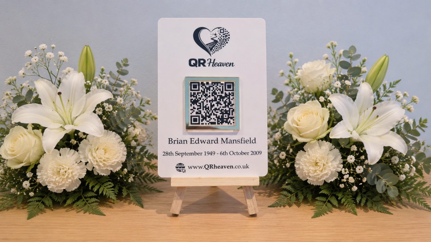 A white QR Heaven memorial plaque on a small easel, surrounded by white lilies, roses and carnations