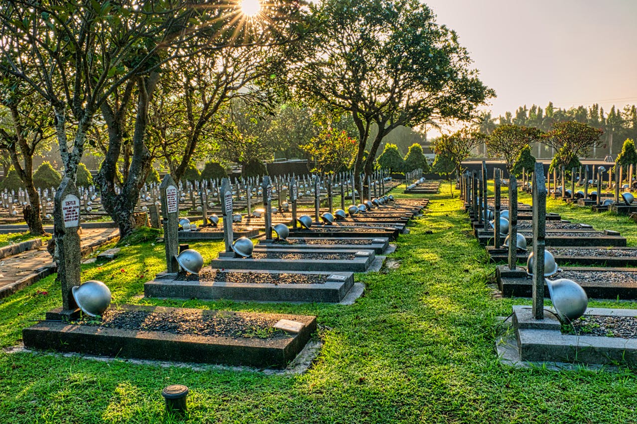 Mastering the First Impression: Your intriguing post title goes here Rows of gravestones with military hardhats located on green tall trees with lush foliage in main heroes cemetery in Indonesia