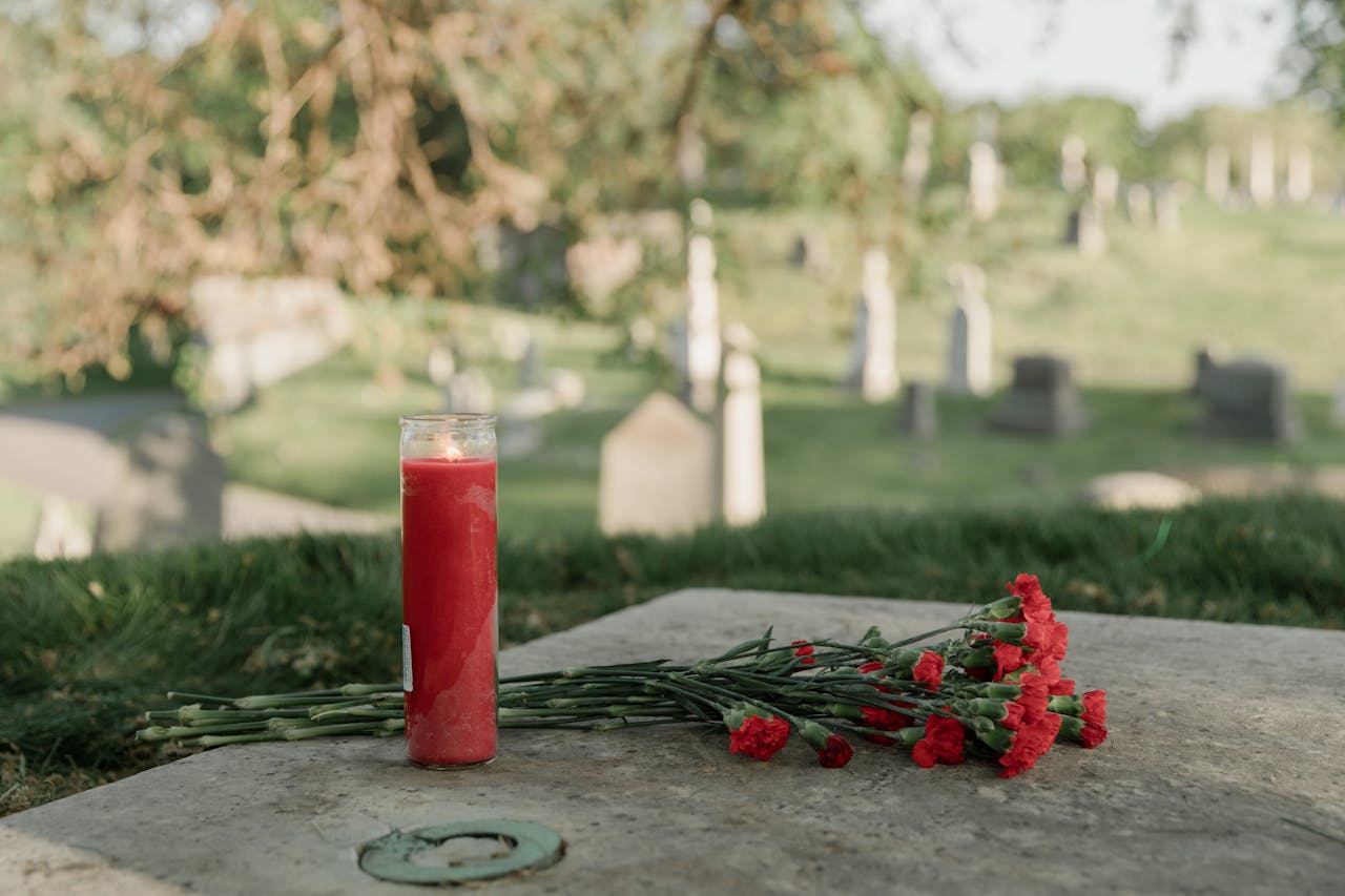 About A serene cemetery scene with a red candle and carnations honoring a memory.